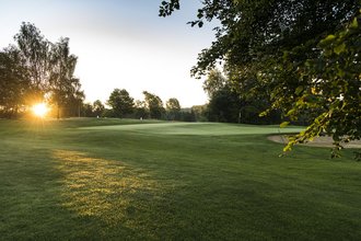 Ein Loch mit Bunker, auf dem Golfplatz des Allgäuer Golf- und Landclub e.V. – zwischen den umliegenden Bäumen und Büschen bricht das Licht der Abendsonne durch und taucht das Green in ein malerisches goldenes Licht (Credit: Stefan von Stengel)